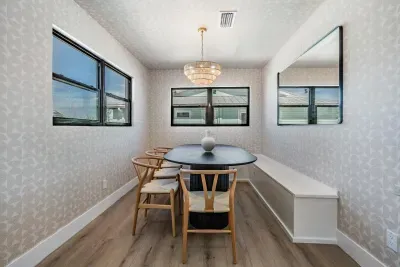 Charming dining nook filled with natural light, featuring elegant wallpaper, a modern chandelier, and cozy built-in seating. Perfect for enjoying family meals or intimate gatherings in a stylish, welcoming coastal setting.
