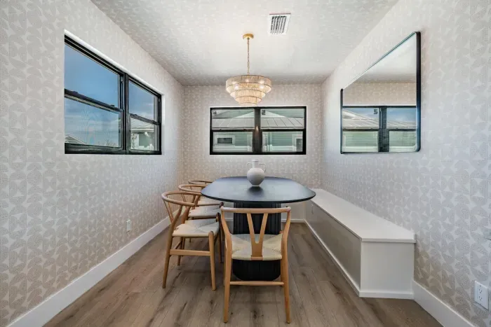 Charming dining nook filled with natural light, featuring elegant wallpaper, a modern chandelier, and cozy built-in seating. Perfect for enjoying family meals or intimate gatherings in a stylish, welcoming coastal setting.