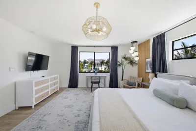 Serene bedroom retreat with plush bedding, elegant lighting, and soft neutral tones. Enjoy a wall-mounted TV, spacious dresser, and cozy seating by the window, creating a bright, relaxing space perfect for unwinding after a long day.
