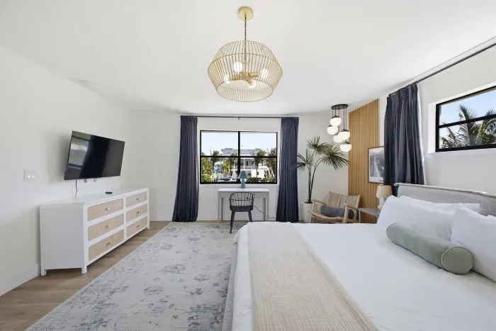 Serene bedroom retreat with plush bedding, elegant lighting, and soft neutral tones. Enjoy a wall-mounted TV, spacious dresser, and cozy seating by the window, creating a bright, relaxing space perfect for unwinding after a long day.