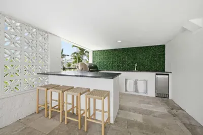 Stylish outdoor bar and kitchen with sleek countertops, bar seating, and lush green accent wall. Perfect for entertaining, grilling, or enjoying drinks poolside in a modern, open-air setting designed for relaxation and fun.