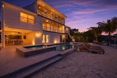 Stunning waterfront retreat at sunset with glowing outdoor lighting, private pool, and sandy lounge area. Relax under the evening sky, enjoy the warm ambiance, and experience the perfect blend of luxury, comfort, and coastal charm.