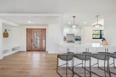 Welcoming open entryway and kitchen featuring stylish pendant lighting, rattan barstools, and warm wood tones. This bright coastal space blends modern design with laid-back charm—perfect for gathering, dining, or unwinding after a beach day.