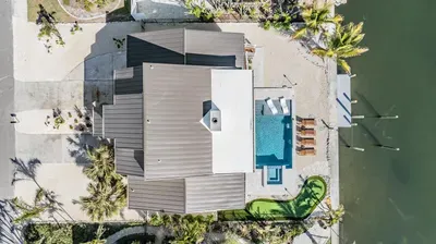 Aerial view of a stunning waterfront oasis featuring a private pool, putting green, and dock. Surrounded by tropical landscaping, this luxurious coastal retreat offers the ultimate blend of relaxation, recreation, and scenic beauty.