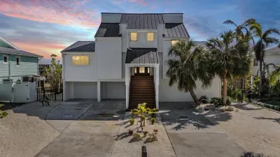 Striking coastal home illuminated at sunset, featuring bold architecture, tropical landscaping, and a welcoming grand entrance. A perfect blend of modern elegance and island charm—your luxurious waterfront getaway begins here.
