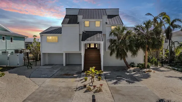 Striking coastal home illuminated at sunset, featuring bold architecture, tropical landscaping, and a welcoming grand entrance. A perfect blend of modern elegance and island charm—your luxurious waterfront getaway begins here.