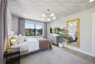 Stylish guest bedroom with large windows, lush views, and natural light. Features a cozy bed, modern décor, and a chic workspace—perfect for relaxing or catching up on work in a serene coastal-inspired setting.