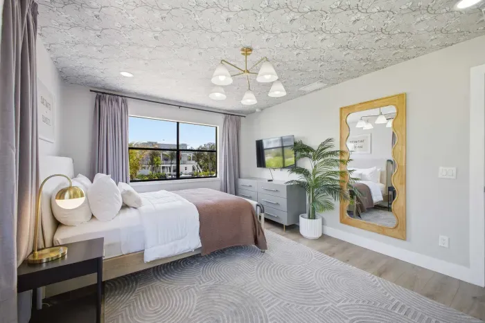 Stylish guest bedroom with large windows, lush views, and natural light. Features a cozy bed, modern décor, and a chic workspace—perfect for relaxing or catching up on work in a serene coastal-inspired setting.