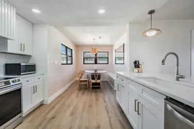 Bright kitchen and dining nook featuring modern white cabinetry, stainless steel appliances, and warm wood floors. The cozy dining area with natural light creates a perfect spot for morning coffee or relaxed meals with family and friends.