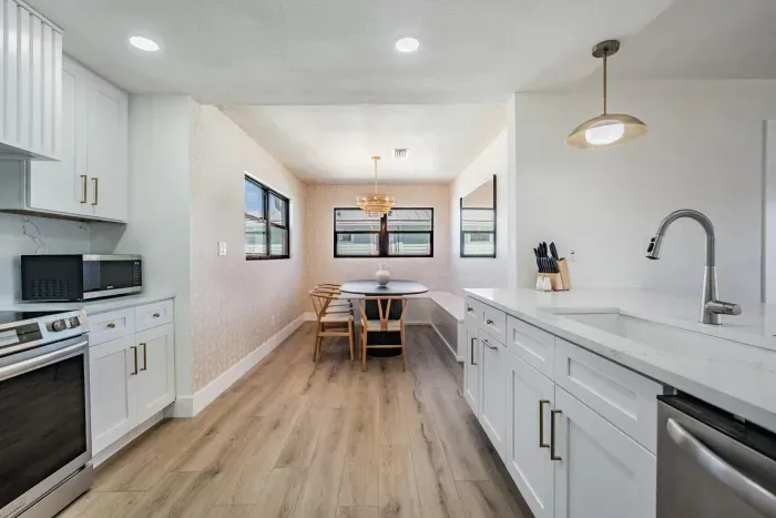 Bright kitchen and dining nook featuring modern white cabinetry, stainless steel appliances, and warm wood floors. The cozy dining area with natural light creates a perfect spot for morning coffee or relaxed meals with family and friends.