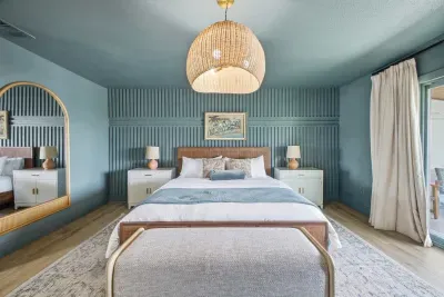 Elegant coastal bedroom with soft blue tones, plush bedding, and stylish wood accents. Relax under warm designer lighting, with matching nightstands and serene décor creating a calm, upscale retreat perfect for restful nights.