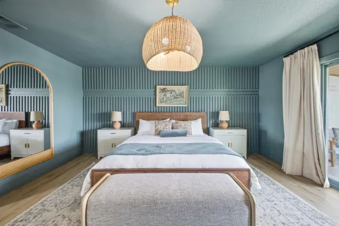 Elegant coastal bedroom with soft blue tones, plush bedding, and stylish wood accents. Relax under warm designer lighting, with matching nightstands and serene décor creating a calm, upscale retreat perfect for restful nights.