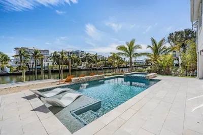 Luxurious waterfront pool with built-in loungers and spa, surrounded by palm trees and canal views. The perfect tropical escape for sunbathing, swimming, or enjoying serene sunsets in paradise.