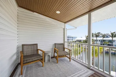 Covered balcony retreat with cozy seating and serene water views. Enjoy your morning coffee or unwind at sunset in this breezy outdoor space, complete with sliding glass doors and a peaceful, private atmosphere perfect for relaxation.
