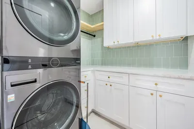 Bright and functional laundry room featuring modern appliances, sleek white cabinetry, and soft green tile backsplash. Stylish and efficient, it’s the perfect blend of design and convenience for extended stays or beach getaways.
