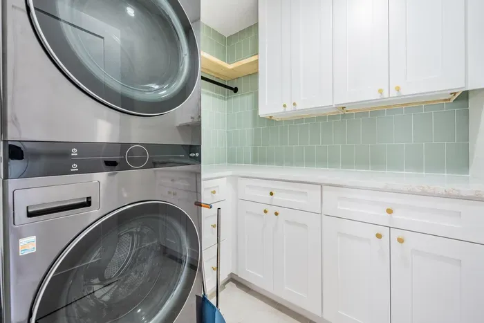 Bright and functional laundry room featuring modern appliances, sleek white cabinetry, and soft green tile backsplash. Stylish and efficient, it’s the perfect blend of design and convenience for extended stays or beach getaways.