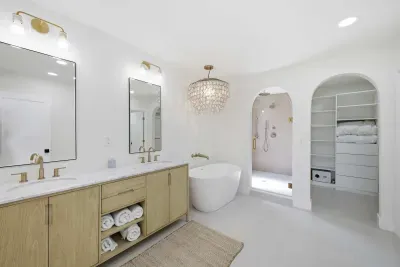 Luxurious spa-inspired bathroom featuring a freestanding soaking tub, double vanity, and walk-in shower with gold fixtures. Bright, airy, and elegant—this retreat blends modern design with coastal serenity for ultimate relaxation.