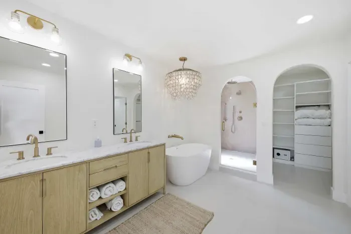Luxurious spa-inspired bathroom featuring a freestanding soaking tub, double vanity, and walk-in shower with gold fixtures. Bright, airy, and elegant—this retreat blends modern design with coastal serenity for ultimate relaxation.