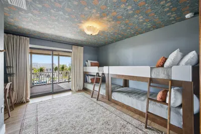 Charming bunk room with cozy built-in beds, playful wallpaper, and sliding doors opening to a balcony with water views. Perfect for kids or groups, this stylish retreat combines comfort, fun, and a touch of tropical flair.