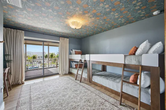 Charming bunk room with cozy built-in beds, playful wallpaper, and sliding doors opening to a balcony with water views. Perfect for kids or groups, this stylish retreat combines comfort, fun, and a touch of tropical flair.