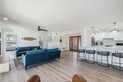 Open-concept living space with chic coastal décor, featuring plush blue sofas, a sleek breakfast bar, and warm wood accents. Perfect for entertaining or relaxing, this bright area flows effortlessly into the kitchen for easy, breezy vacation living.