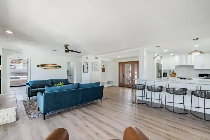 Open-concept living space with chic coastal décor, featuring plush blue sofas, a sleek breakfast bar, and warm wood accents. Perfect for entertaining or relaxing, this bright area flows effortlessly into the kitchen for easy, breezy vacation living.