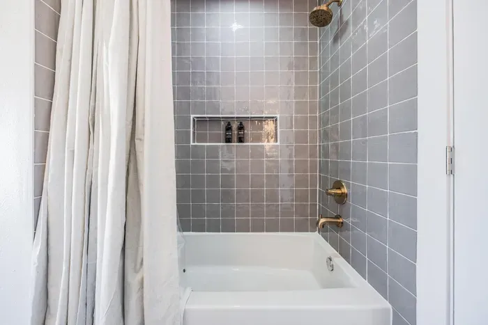 Chic shower-tub combo with sleek gray tile and gold fixtures. Modern and inviting, this space offers a perfect blend of style and comfort for a refreshing coastal-inspired bath experience.