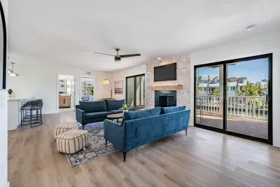 Spacious and sunlit living area with modern coastal flair—featuring plush seating, a stone fireplace, and sliding doors that open to water-view balconies. Ideal for relaxing, entertaining, or soaking up the serene tropical surroundings.
