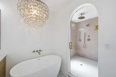 Elegant ensuite featuring a freestanding soaking tub and spacious walk-in shower with dual rain heads. Gold accents and soft neutral tones create a spa-like atmosphere—perfect for unwinding in comfort and coastal luxury.
