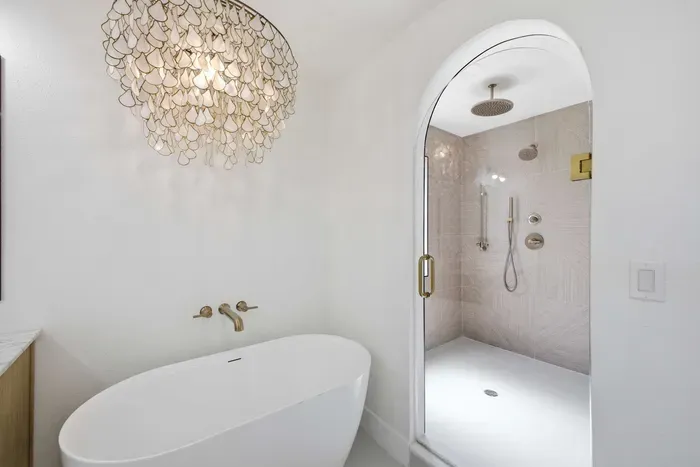 Elegant ensuite featuring a freestanding soaking tub and spacious walk-in shower with dual rain heads. Gold accents and soft neutral tones create a spa-like atmosphere—perfect for unwinding in comfort and coastal luxury.