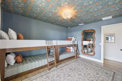 Fun and stylish bunk room with cozy twin beds, playful wallpaper ceiling, and charming décor. Perfect for kids or groups, featuring soft bedding, unique mirror accents, and a bright, inviting space designed for comfort and relaxation.