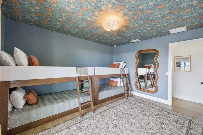 Fun and stylish bunk room with cozy twin beds, playful wallpaper ceiling, and charming décor. Perfect for kids or groups, featuring soft bedding, unique mirror accents, and a bright, inviting space designed for comfort and relaxation.
