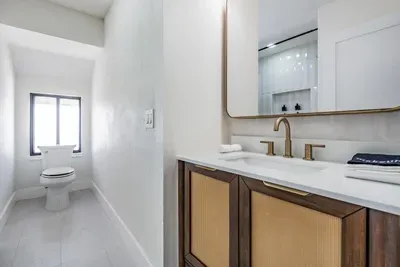 Sleek bathroom with modern coastal charm, featuring a rattan-accent vanity, gold fixtures, and a bright, airy layout. Simple elegance meets functionality for a refreshing and stylish retreat.