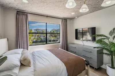 Cozy guest bedroom with serene canal views, soft natural tones, and modern décor. Featuring a plush bed, smart TV, and tropical accents, this peaceful retreat is perfect for relaxing after a sun-filled day.