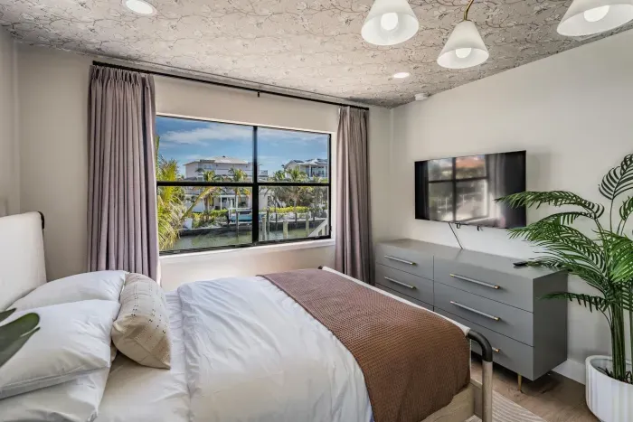 Cozy guest bedroom with serene canal views, soft natural tones, and modern décor. Featuring a plush bed, smart TV, and tropical accents, this peaceful retreat is perfect for relaxing after a sun-filled day.