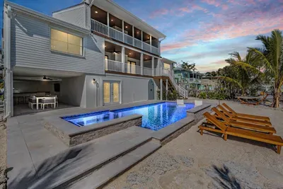 Chic coastal retreat featuring a glowing infinity pool, spa, and sleek sun loungers steps from the water. Enjoy open-air dining under the covered patio or sunset views from private balconies—perfect for relaxing in modern luxury by the canal.