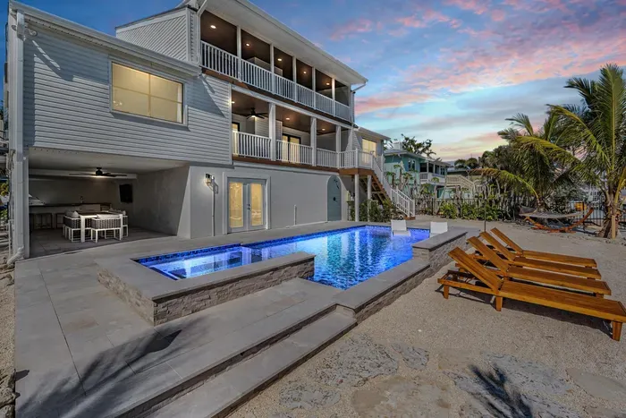 Chic coastal retreat featuring a glowing infinity pool, spa, and sleek sun loungers steps from the water. Enjoy open-air dining under the covered patio or sunset views from private balconies—perfect for relaxing in modern luxury by the canal.