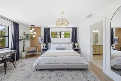 Serene primary suite with modern coastal design, featuring a plush king bed, elegant lighting, and soothing tones. Natural light and refined décor create a peaceful retreat—complete with a private ensuite for ultimate comfort and relaxation.
