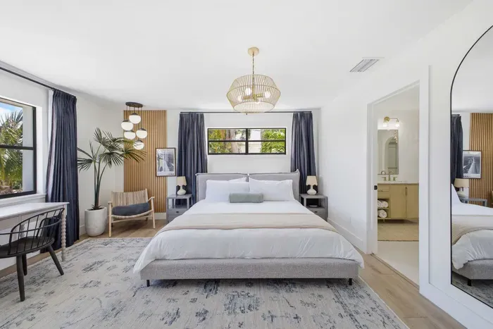 Serene primary suite with modern coastal design, featuring a plush king bed, elegant lighting, and soothing tones. Natural light and refined décor create a peaceful retreat—complete with a private ensuite for ultimate comfort and relaxation.