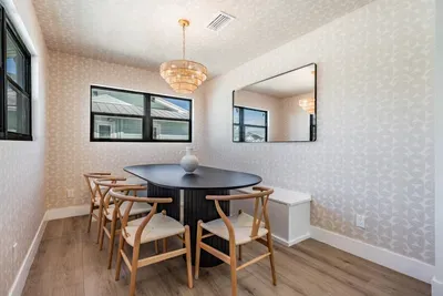 Stylish dining room with coastal flair, featuring a round table, chic chandelier, and bench seating framed by sunlit windows. Perfect for shared meals or game nights in a bright, inviting space that blends elegance and comfort.