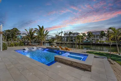 Luxury waterfront paradise with a glowing pool, spa, and sun deck overlooking a serene canal. Lounge under palm trees or unwind in the hot tub as the sunset paints the sky—an idyllic escape blending elegance, comfort, and tropical charm.
