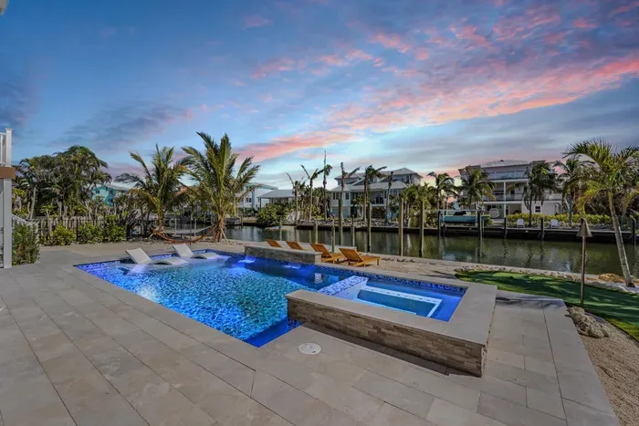 Luxury waterfront paradise with a glowing pool, spa, and sun deck overlooking a serene canal. Lounge under palm trees or unwind in the hot tub as the sunset paints the sky—an idyllic escape blending elegance, comfort, and tropical charm.