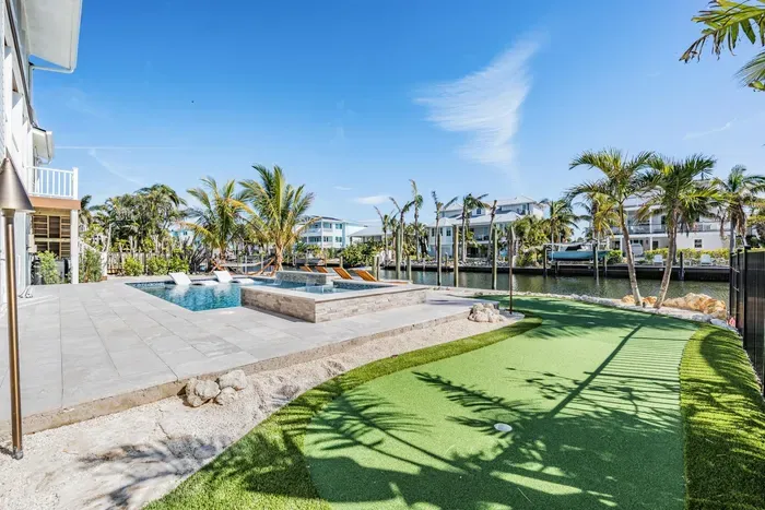 Tropical backyard paradise featuring a sparkling pool, spa, and private putting green. Overlooking a peaceful canal, this vibrant outdoor space is perfect for relaxing, entertaining, or enjoying fun in the Florida sun.