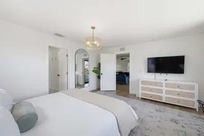 Spacious, light-filled bedroom with plush bedding, sleek dresser, and wall-mounted TV. Soft tones and elegant lighting create a calming retreat, with easy access to the ensuite bath for added comfort and convenience.