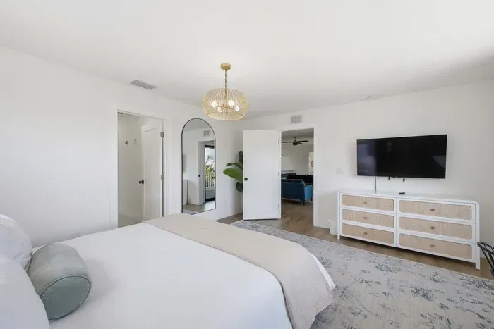 Spacious, light-filled bedroom with plush bedding, sleek dresser, and wall-mounted TV. Soft tones and elegant lighting create a calming retreat, with easy access to the ensuite bath for added comfort and convenience.