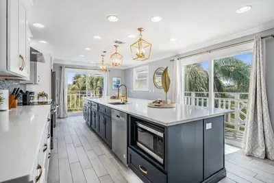 Bright & modern chef’s kitchen with sleek cabinetry, quartz counters, and a grand island with seating. Floor-to-ceiling windows fill the space with natural light and tropical views—perfect for cooking, entertaining & gathering.