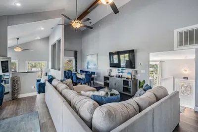 Cozy yet spacious living room featuring a large sectional, vaulted ceilings with exposed beams, and modern décor. Perfect for family movie nights, game time, or simply relaxing while enjoying natural light & water views.
