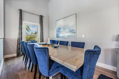 Sophisticated dining room with a polished wooden table, luxe navy velvet chairs, and chic coastal décor. Bathed in natural light, it’s the perfect space to gather for family meals, celebrations, or elegant dinner parties.