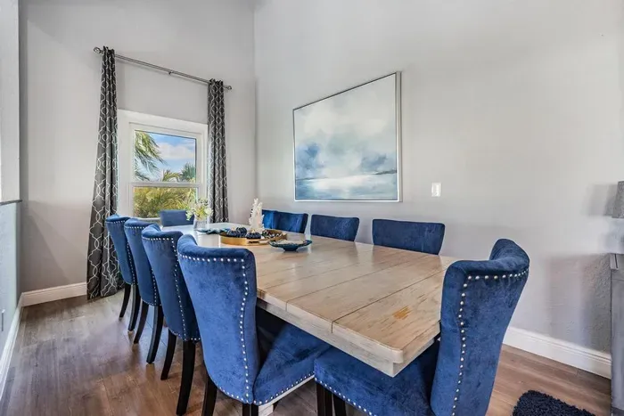 Sophisticated dining room with a polished wooden table, luxe navy velvet chairs, and chic coastal décor. Bathed in natural light, it’s the perfect space to gather for family meals, celebrations, or elegant dinner parties.