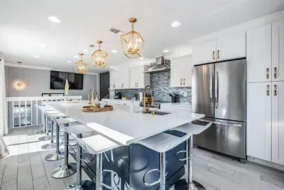 This kitchen showcases a massive island with seating for 8, stainless steel appliances, quartz counters & gold accents. Perfect for family meals, entertaining guests, or enjoying morning coffee in a bright, open space.